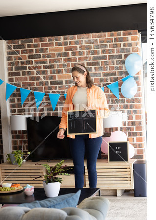 Woman holding chalkboard at gender reveal party, smiling and celebrating indoors 135634798