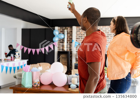 Friends celebrating at home with decorations, capturing memories on smartphone 135634800