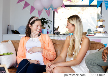 Pregnant woman smiling and chatting with friend at baby shower celebration Pregnant woman smiling and chatting with friend at baby shower celebration 135634804