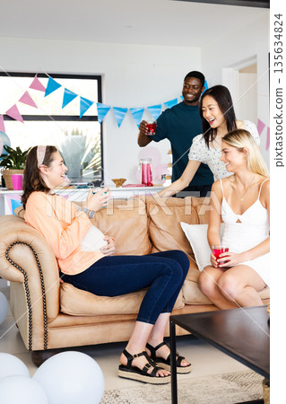 Friends celebrating at home, enjoying drinks and laughter on cozy sofa 135634824
