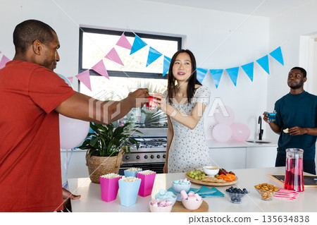 Friends celebrating at home, enjoying snacks and drinks with festive decorations Friends celebrating at home, enjoying snacks and drinks with festive decorations 135634838