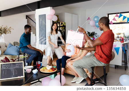 Friends celebrating baby shower at home, giving gifts and enjoying snacks together Friends celebrating baby shower at home, giving gifts and enjoying snacks together 135634850