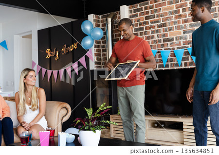 Friends playing baby shower game with chalkboard, enjoying festive indoor gathering 135634851