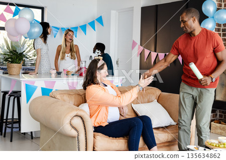 African American man handing gift to pregnant woman at home baby shower celebration 135634862