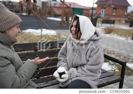 Close Friends Talk and Enjoy Warm Drinks in a Park During Winter Afternoon Close Friends Talk and Enjoy Warm Drinks in a Park During Winter Afternoon 135635092