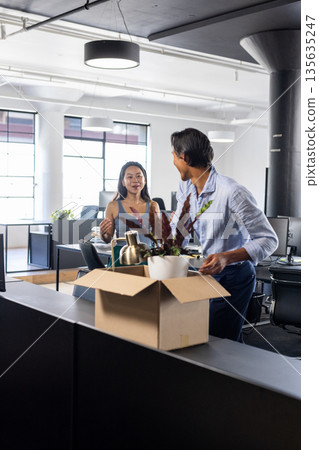 Colleagues in modern office unpacking boxes and discussing new workspace setup 135635247