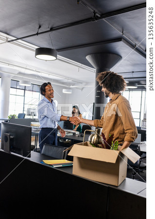 Colleagues shaking hands in modern office, welcoming new team member with box 135635248
