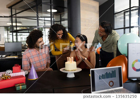 In office, colleagues gathering around woman with cake and gifts for birthday 135635250