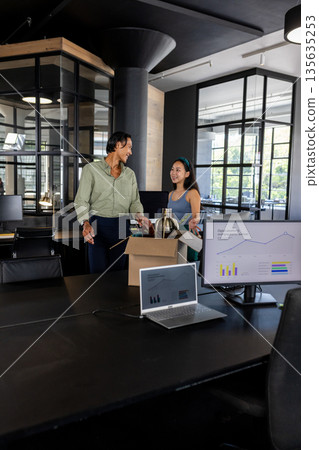 Colleagues discussing project while unpacking box in modern office workspace 135635253