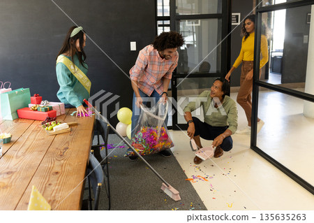 Colleagues cleaning up after office celebration, smiling and enjoying teamwork 135635263