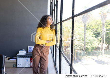 Gazing thoughtfully out office window, businesswoman in yellow sweater contemplating ideas 135635285