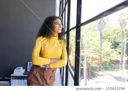 Confident woman in yellow sweater looking out office window, planning future goals Confident woman in yellow sweater looking out office window, planning future goals 135635294