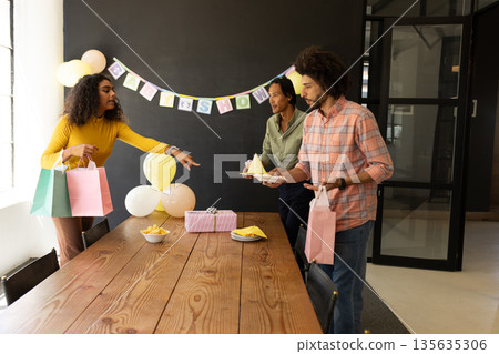 Colleagues preparing for celebration, arranging gifts and snacks on office table Colleagues preparing for celebration, arranging gifts and snacks on office table 135635306