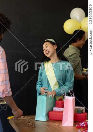 Asian woman at baby shower smiling with gifts and balloons on table Asian woman at baby shower smiling with gifts and balloons on table 135635309