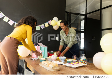 Colleagues preparing party table with snacks and gifts in modern office 135635320