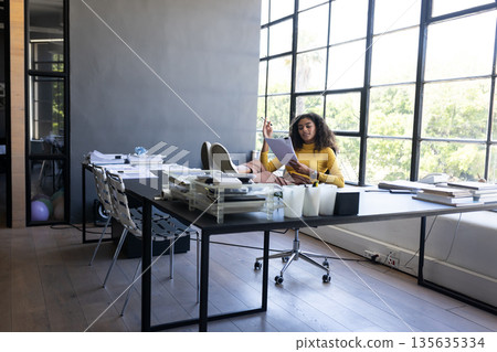 Young woman in office reading documents with feet up on desk, relaxing 135635334