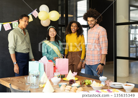 Colleagues celebrating with gifts and decorations at office party, smiling together 135635349