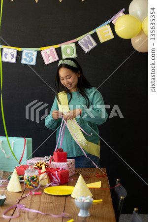 Smiling woman preparing gifts at baby shower party with colorful decorations Smiling woman preparing gifts at baby shower party with colorful decorations 135635354
