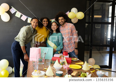 Diverse group celebrating baby shower with gifts and decorations in office 135635356