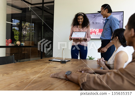 Smiling woman presenting award to colleagues in modern office meeting room Smiling woman presenting award to colleagues in modern office meeting room 135635357