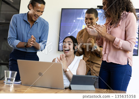 Diverse business team celebrating success while looking at laptop in modern office Diverse business team celebrating success while looking at laptop in modern office 135635358