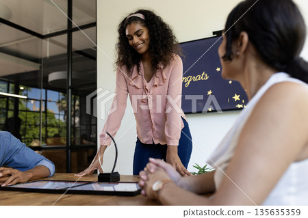Smiling woman presenting award in modern office meeting with colleagues Smiling woman presenting award in modern office meeting with colleagues 135635359