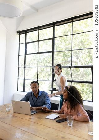 Business team collaborating on laptop in bright office, discussing project ideas 135635383