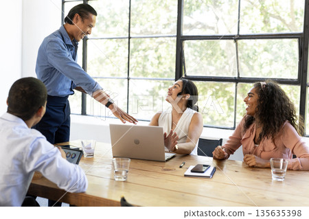 In meeting, diverse team discussing ideas around laptop, collaborating and smiling 135635398