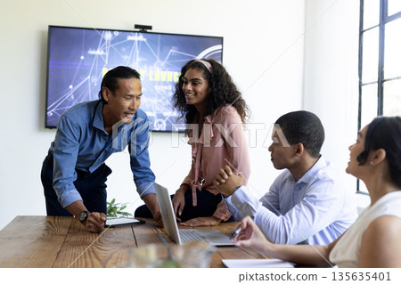Diverse business team collaborating in modern office, discussing project on laptop Diverse business team collaborating in modern office, discussing project on laptop 135635401