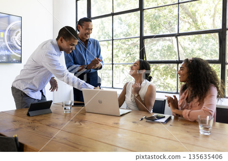 Diverse business team collaborating at office, discussing ideas around laptop 135635406