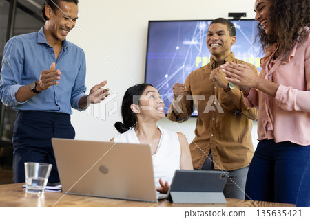 Diverse business team celebrating success with laptop and tablet in modern office Diverse business team celebrating success with laptop and tablet in modern office 135635421