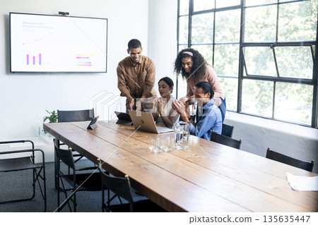 Diverse business team collaborating on laptops during office meeting, sharing ideas 135635447