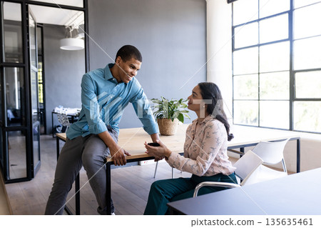 African American man and woman discussing work in modern office, smiling and engaged African American man and woman discussing work in modern office, smiling and engaged 135635461
