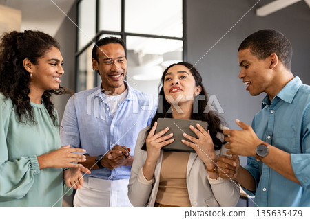 Diverse business team celebrating success with tablet in modern office setting Diverse business team celebrating success with tablet in modern office setting 135635479