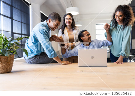 Diverse business team celebrating success around laptop in modern office 135635482