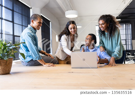 Diverse business team collaborating around laptop in modern office, sharing ideas Diverse business team collaborating around laptop in modern office, sharing ideas 135635516