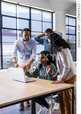 Celebrating success, diverse business team collaborating on laptop in modern office Celebrating success, diverse business team collaborating on laptop in modern office 135635517
