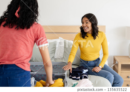 Mother and daughter packing suitcase on bed, preparing for family trip Mother and daughter packing suitcase on bed, preparing for family trip 135635522