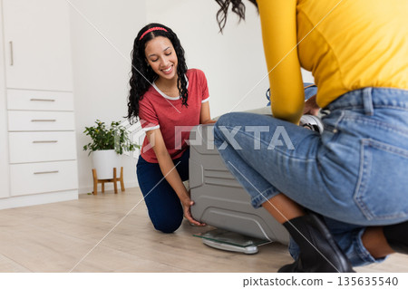 Mother and daughter packing suitcase together at home, preparing for travel 135635540