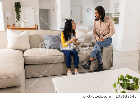 Discussing documents, African American mother and child smiling warmly on living room sofa 135635543