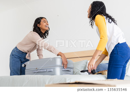 African American mother and daughter packing suitcase on bed, smiling and laughing African American mother and daughter packing suitcase on bed, smiling and laughing 135635546
