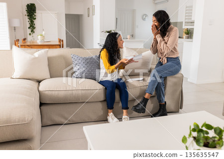 Mother and daughter sharing exciting news at home, both looking joyful and surprised 135635547