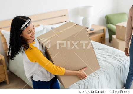African American woman carrying cardboard box in bedroom, smiling and organizing 135635553
