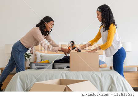 African American mother and daughter packing boxes on bed, preparing for move African American mother and daughter packing boxes on bed, preparing for move 135635555