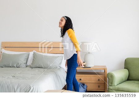 Smiling woman standing in bedroom holding smartphone, enjoying moment of relaxation Smiling woman standing in bedroom holding smartphone, enjoying moment of relaxation 135635559