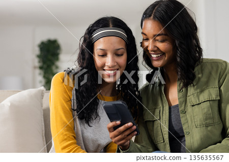 Mother and daughter smiling while looking at smartphone together at home Mother and daughter smiling while looking at smartphone together at home 135635567