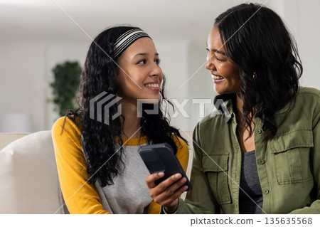 Smiling, African American mother and daughter looking at smartphone together at home 135635568