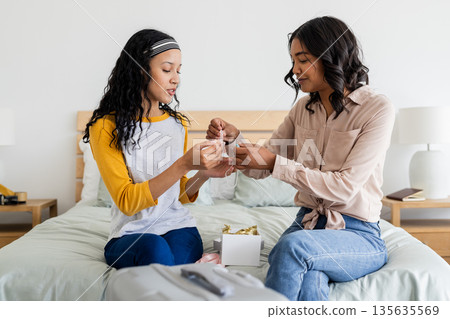 Mother and daughter wrapping gift together on bed, sharing joyful moment 135635569