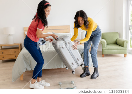 African American women packing suitcase together in bedroom, preparing for travel African American women packing suitcase together in bedroom, preparing for travel 135635584
