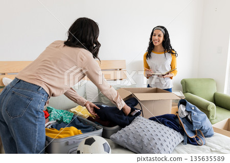 Mother and daughter packing suitcase and boxes, preparing for trip together 135635589